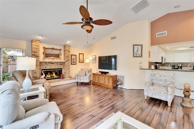 living room featuring ceiling fan, wood-type flooring, high vaulted ceiling, and a brick fireplace