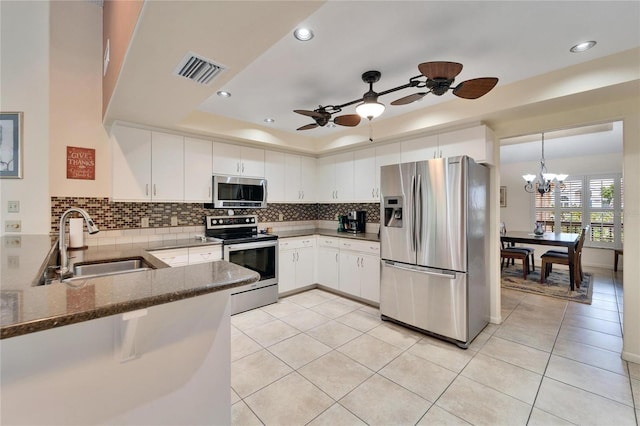 kitchen featuring a raised ceiling, kitchen peninsula, sink, appliances with stainless steel finishes, and white cabinetry