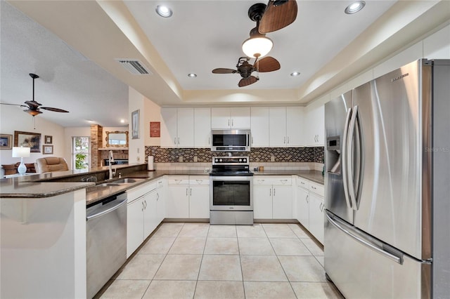 kitchen with a raised ceiling, kitchen peninsula, white cabinets, and appliances with stainless steel finishes