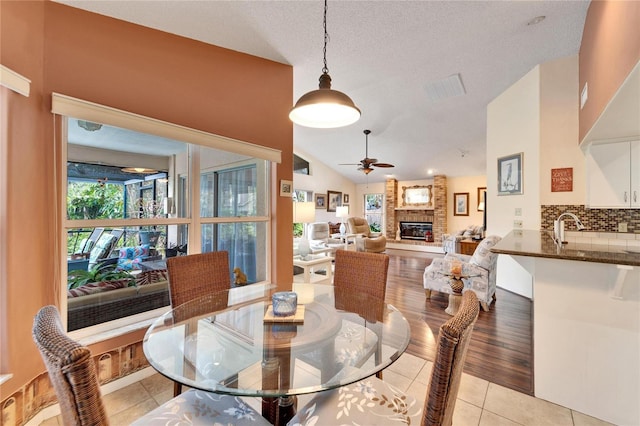 tiled dining room with a textured ceiling, a stone fireplace, ceiling fan, and vaulted ceiling