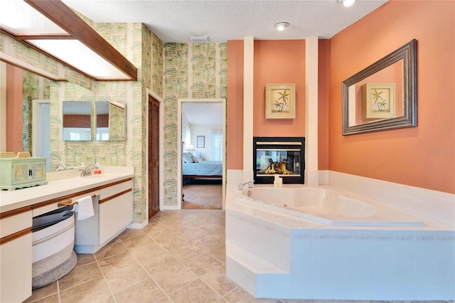 bathroom featuring a multi sided fireplace, vanity, a relaxing tiled tub, and a textured ceiling