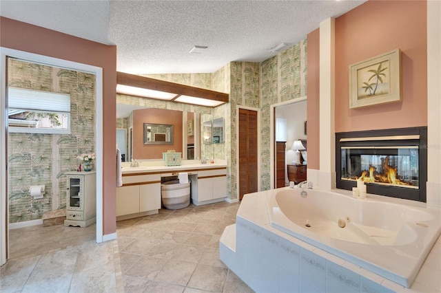 bathroom featuring tile patterned floors, a textured ceiling, vanity, tiled tub, and a multi sided fireplace