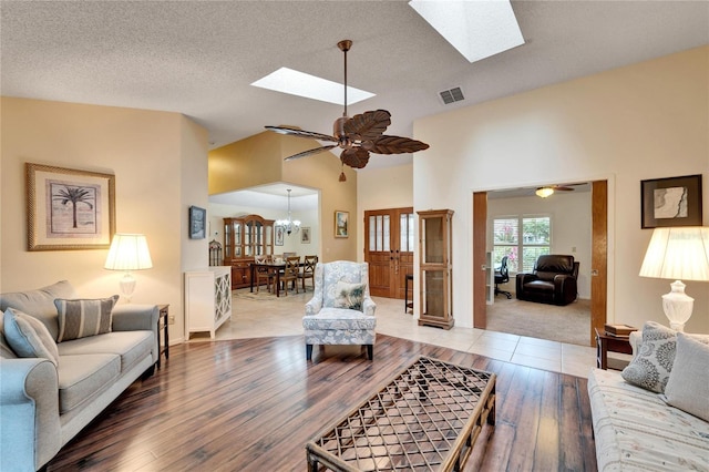 living room with ceiling fan with notable chandelier, wood-type flooring, a textured ceiling, and lofted ceiling with skylight