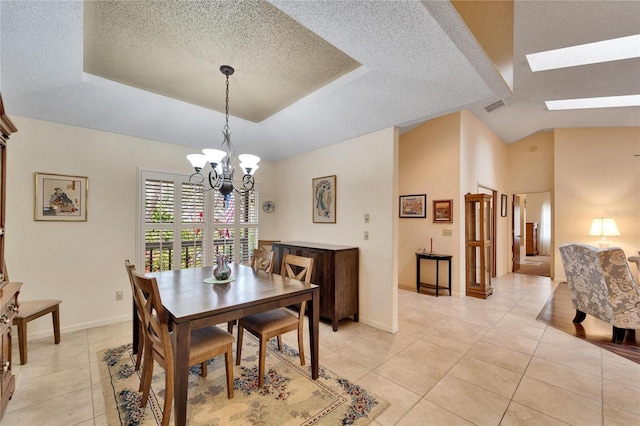 tiled dining room featuring vaulted ceiling with skylight, an inviting chandelier, a textured ceiling, and a tray ceiling