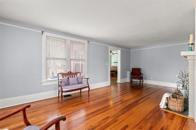 sitting room with ceiling fan, a brick fireplace, and hardwood / wood-style flooring