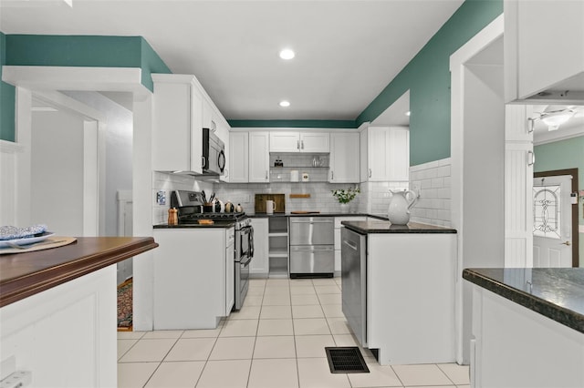 kitchen featuring stainless steel appliances, light tile patterned floors, decorative backsplash, white cabinets, and dark stone countertops