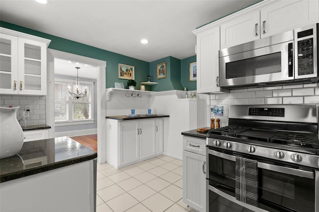 kitchen featuring stainless steel appliances, light tile patterned floors, white cabinets, an inviting chandelier, and backsplash