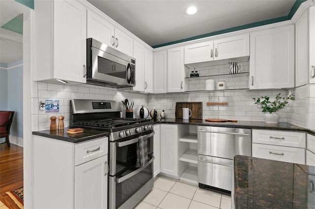 kitchen featuring dark stone countertops, appliances with stainless steel finishes, light tile patterned flooring, white cabinetry, and backsplash