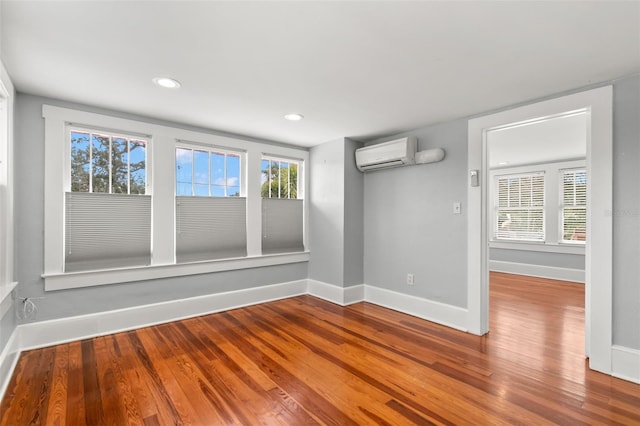 unfurnished room featuring hardwood / wood-style flooring, a wall unit AC, and a wealth of natural light