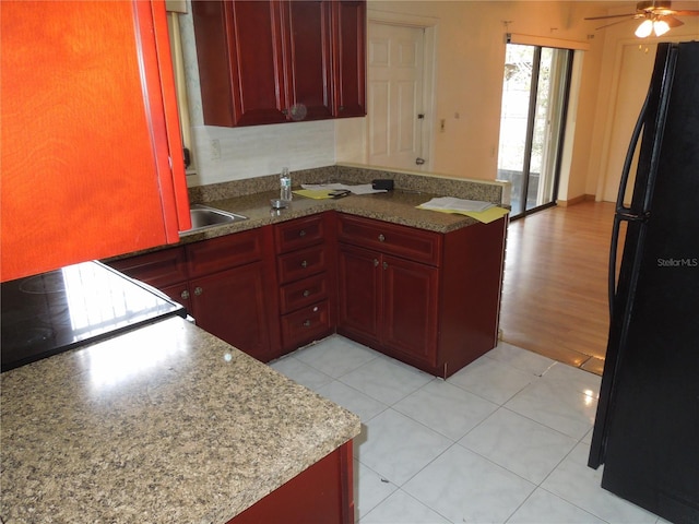 kitchen featuring black refrigerator, stovetop, kitchen peninsula, ceiling fan, and light tile patterned floors