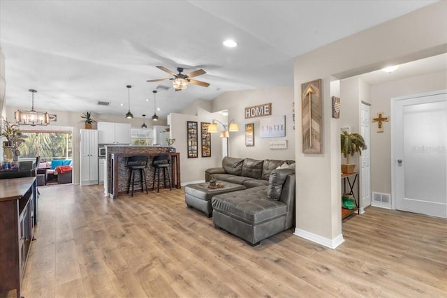 living room featuring light hardwood / wood-style flooring, vaulted ceiling, and ceiling fan with notable chandelier