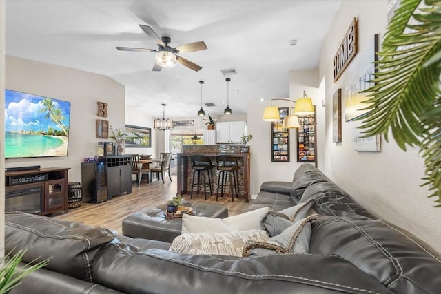 living room with ceiling fan with notable chandelier, wood-type flooring, and lofted ceiling