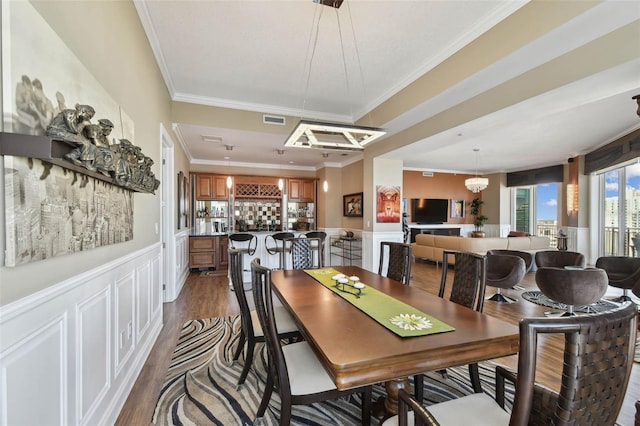 dining area with indoor bar, ornamental molding, dark wood-type flooring, and a chandelier