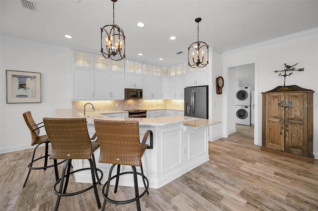 kitchen featuring kitchen peninsula, stainless steel appliances, an inviting chandelier, stacked washer and clothes dryer, and white cabinets