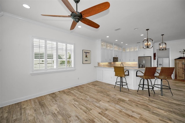 kitchen with stainless steel fridge with ice dispenser, kitchen peninsula, crown molding, a breakfast bar area, and white cabinets