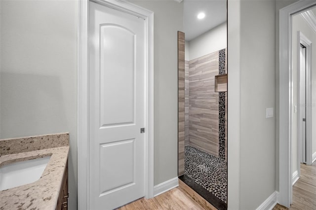 bathroom with hardwood / wood-style flooring, vanity, and a tile shower