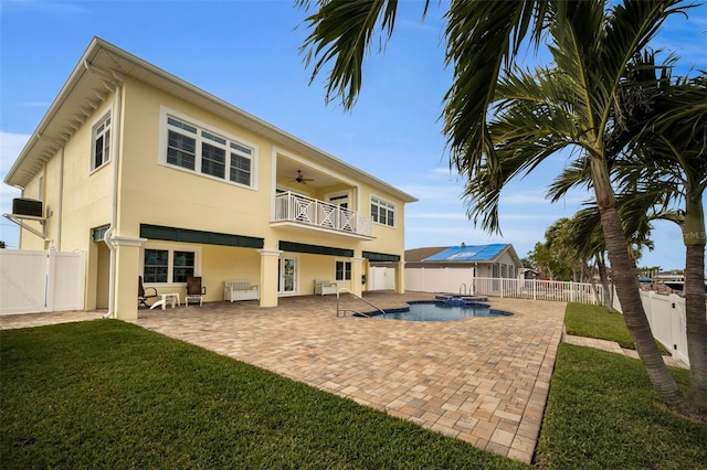 back of property with ceiling fan, a yard, a pool with hot tub, a balcony, and a patio area