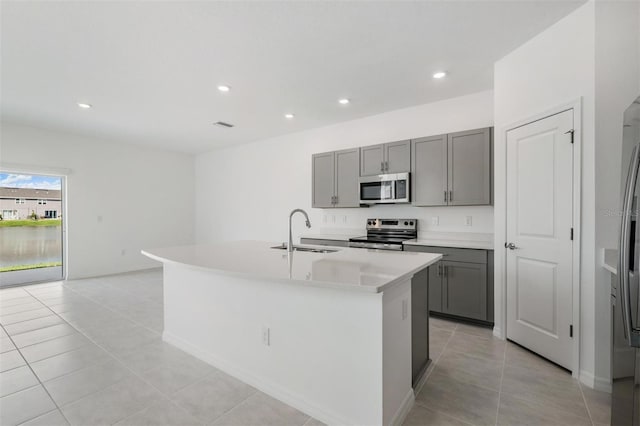 kitchen with appliances with stainless steel finishes, gray cabinetry, an island with sink, and sink