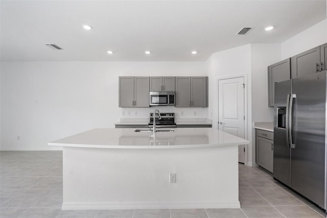 kitchen with sink, light tile patterned floors, a center island with sink, gray cabinetry, and appliances with stainless steel finishes