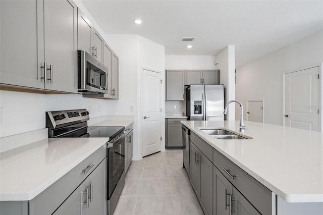 kitchen featuring sink, light tile patterned floors, gray cabinets, a kitchen island with sink, and appliances with stainless steel finishes