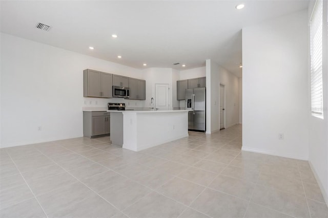 kitchen with sink, light tile patterned floors, an island with sink, gray cabinetry, and appliances with stainless steel finishes