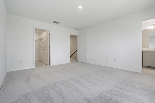 unfurnished bedroom featuring a walk in closet, light carpet, a closet, and connected bathroom