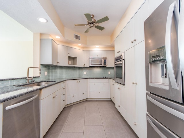 kitchen featuring sink, stainless steel appliances, dark stone countertops, decorative backsplash, and white cabinets