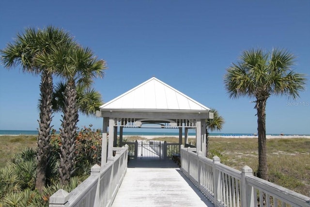 dock area with a gazebo, a water view, and a beach view