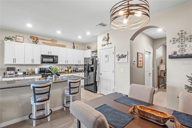 kitchen featuring black appliances, a kitchen breakfast bar, white cabinets, dark stone countertops, and decorative light fixtures