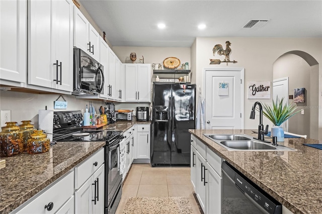 kitchen with dark stone counters, sink, black appliances, white cabinetry, and light tile patterned flooring