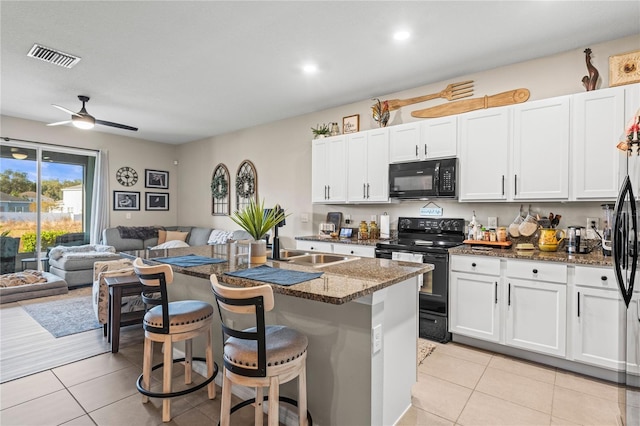 kitchen featuring white cabinetry, a kitchen breakfast bar, a center island with sink, light tile patterned floors, and black appliances