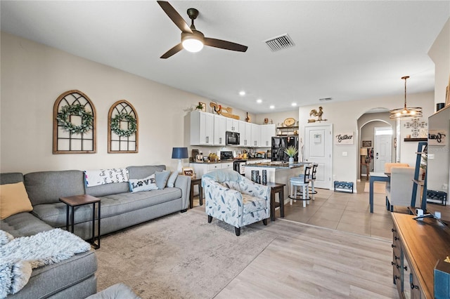 living room featuring ceiling fan with notable chandelier and light hardwood / wood-style floors