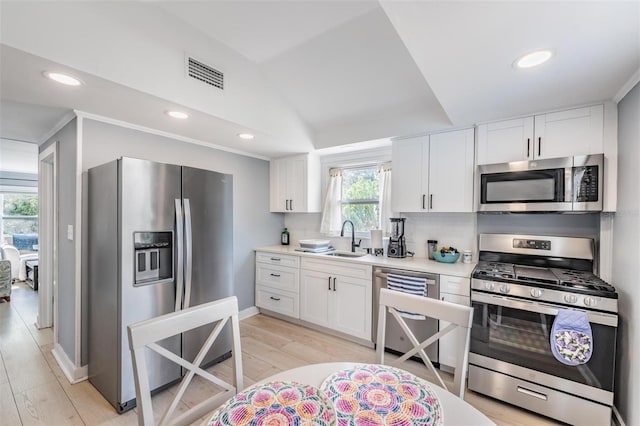 kitchen featuring stainless steel appliances, lofted ceiling, white cabinetry, plenty of natural light, and sink