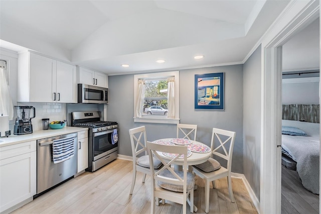 kitchen featuring light hardwood / wood-style flooring, tasteful backsplash, lofted ceiling, white cabinets, and appliances with stainless steel finishes