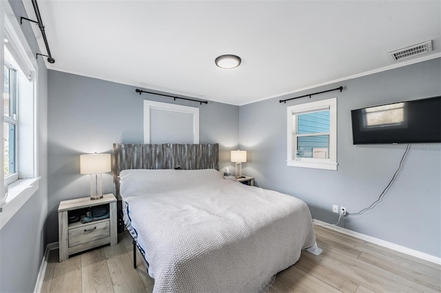 bedroom featuring ornamental molding, light wood-type flooring, and multiple windows