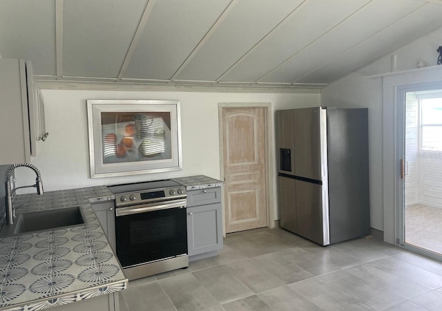 kitchen featuring gray cabinetry, lofted ceiling, sink, light tile patterned flooring, and stainless steel appliances