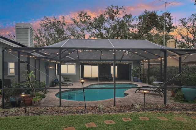 pool at dusk with a patio and glass enclosure