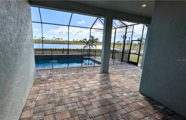 view of pool featuring glass enclosure, a water view, and a patio