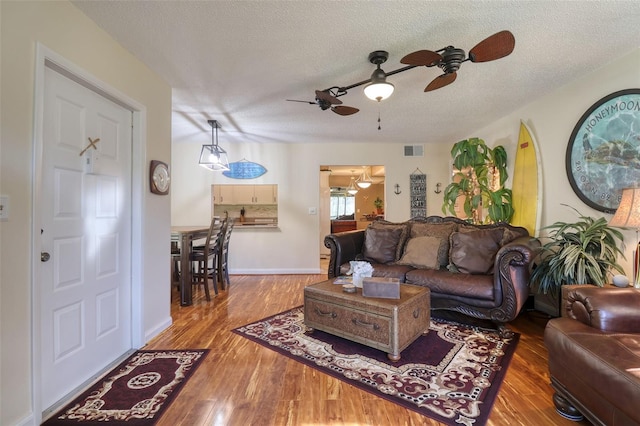 living room with ceiling fan, a textured ceiling, and light hardwood / wood-style floors