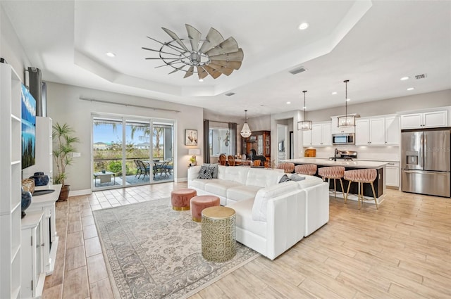 living room featuring ceiling fan, a raised ceiling, and light wood-type flooring