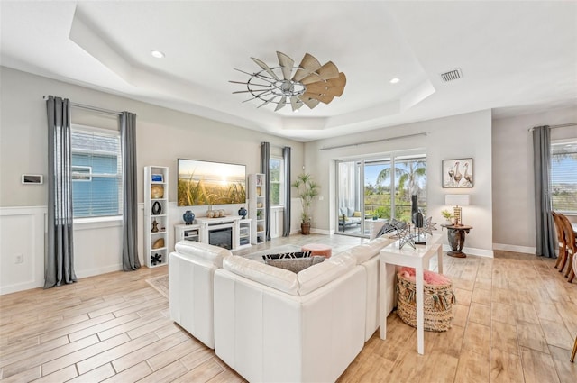 living room with a raised ceiling, ceiling fan, a healthy amount of sunlight, and light hardwood / wood-style floors