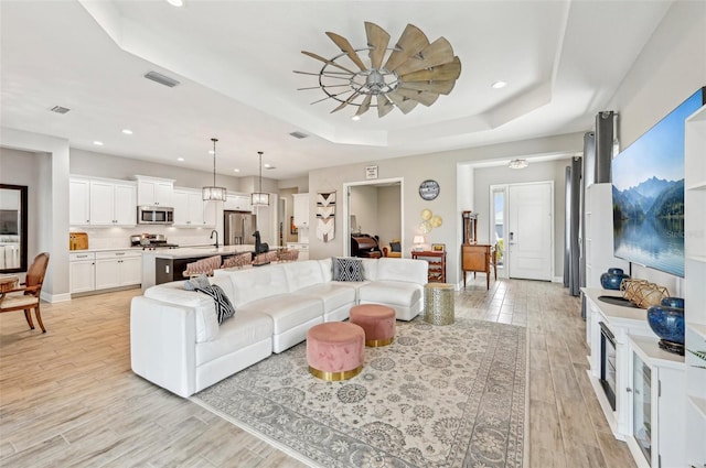 living room with a raised ceiling, sink, and light hardwood / wood-style flooring