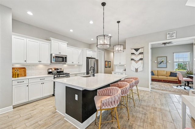 kitchen with pendant lighting, appliances with stainless steel finishes, a kitchen island with sink, and white cabinets