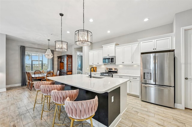 kitchen featuring appliances with stainless steel finishes, decorative light fixtures, white cabinetry, sink, and a center island with sink