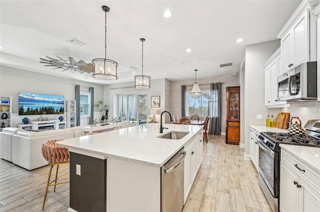 kitchen with appliances with stainless steel finishes, pendant lighting, sink, white cabinets, and a kitchen island with sink