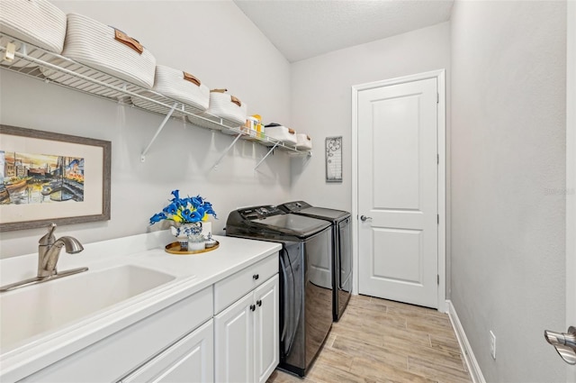 clothes washing area with sink, cabinets, washer and dryer, a textured ceiling, and light wood-type flooring