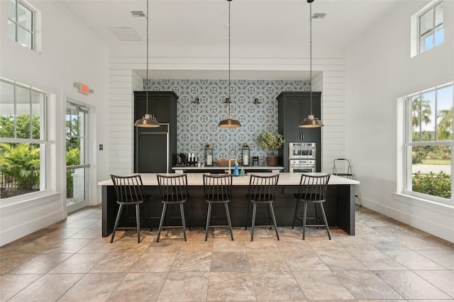 kitchen with a breakfast bar, decorative light fixtures, plenty of natural light, stainless steel double oven, and a kitchen island with sink