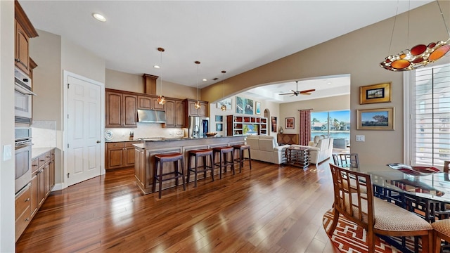 kitchen with a breakfast bar, stainless steel appliances, ceiling fan, decorative light fixtures, and a kitchen island