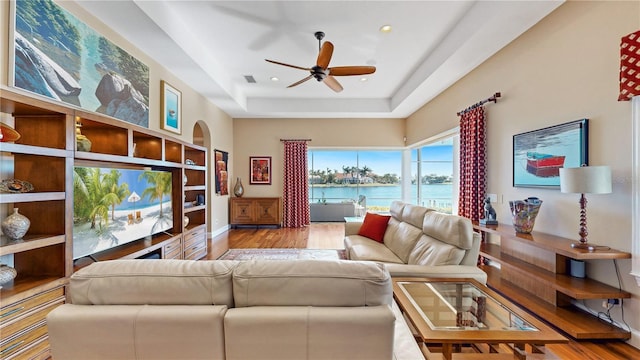 living room featuring a tray ceiling, ceiling fan, and light hardwood / wood-style floors