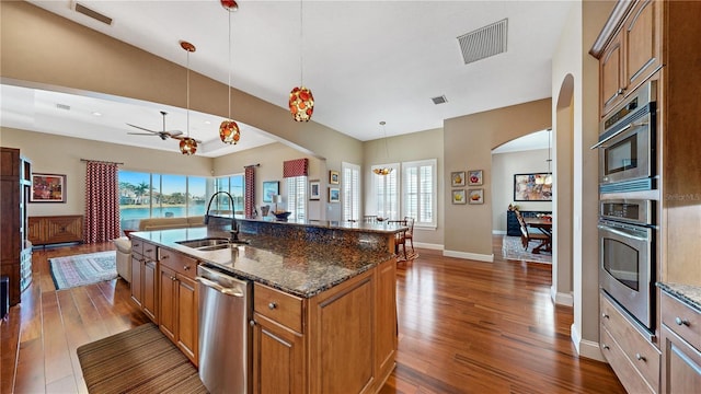 kitchen featuring stainless steel appliances, a kitchen island with sink, sink, decorative light fixtures, and dark stone countertops